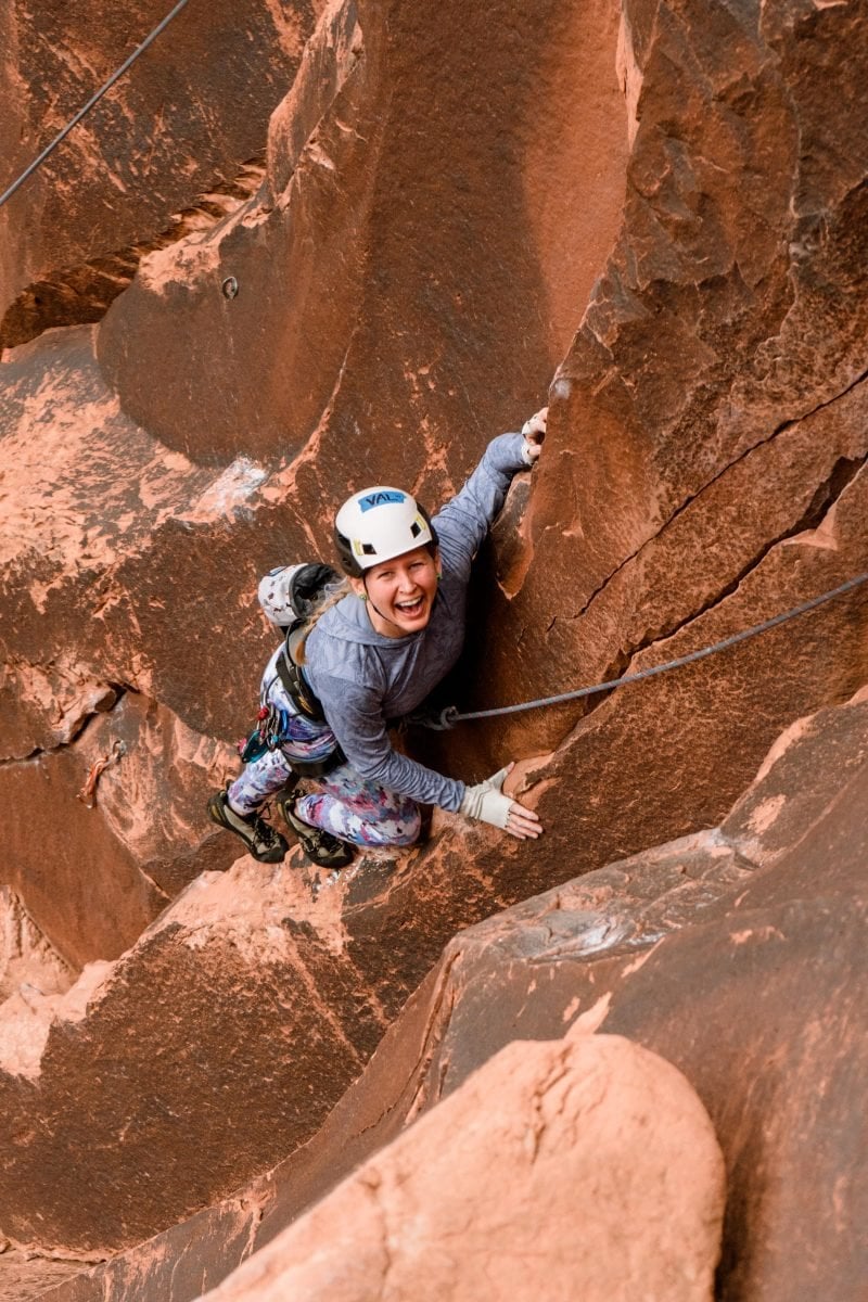 A woman rock climbing and looking up to smile