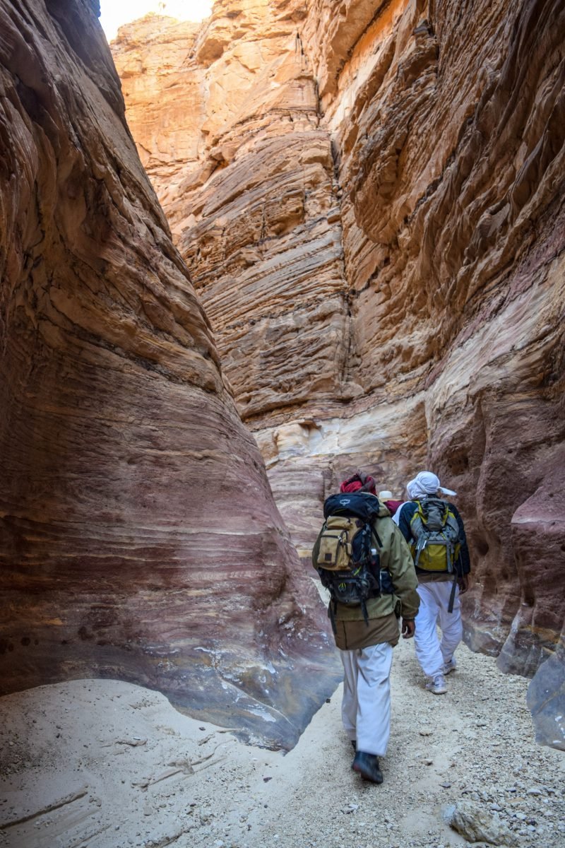 A group of people walking through a narrow canyon in backpacking gear