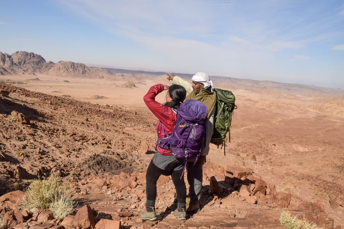 Two backpackers looking on into the distance, one pointing at something for the other to direct their attention to