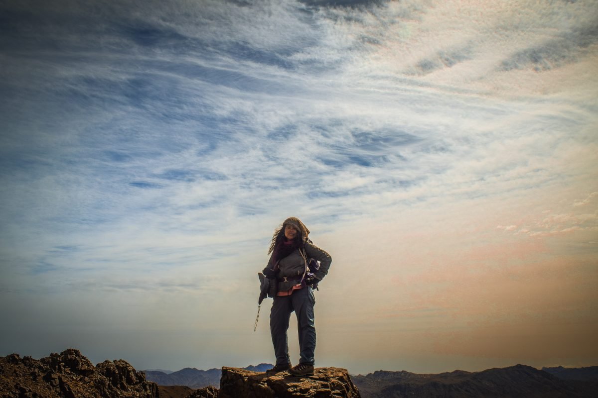 A woman standing on a rocky overlook, a hazy sky behind her, wearing her backpacking gear