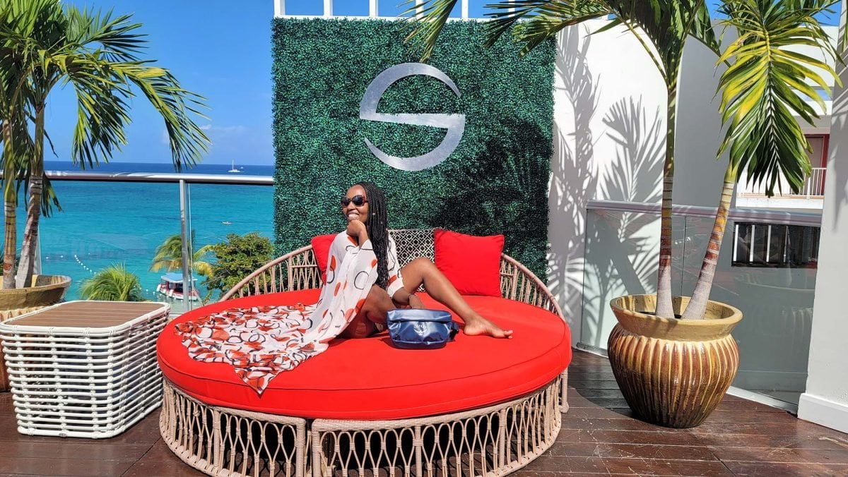 A woman sitting on a red circle chair wearing a white coverup with tropical ocean in the background