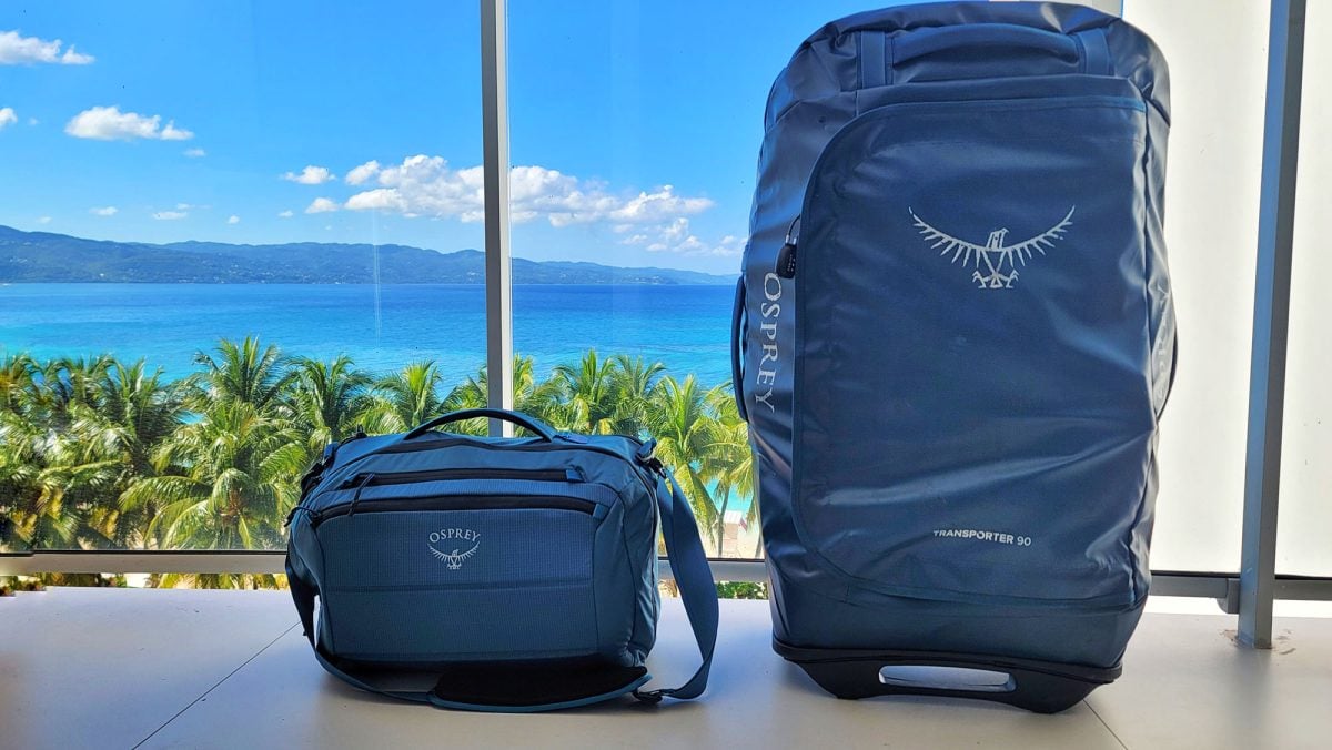 Two blue Osprey travel bags with a tropical view in the background