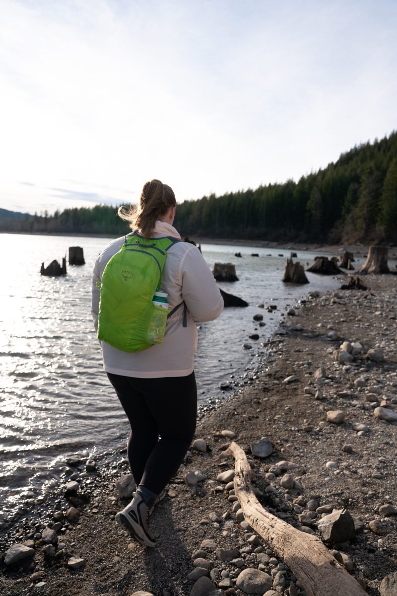 A woman walking along a rocky beach wearing a neon stuff backpack