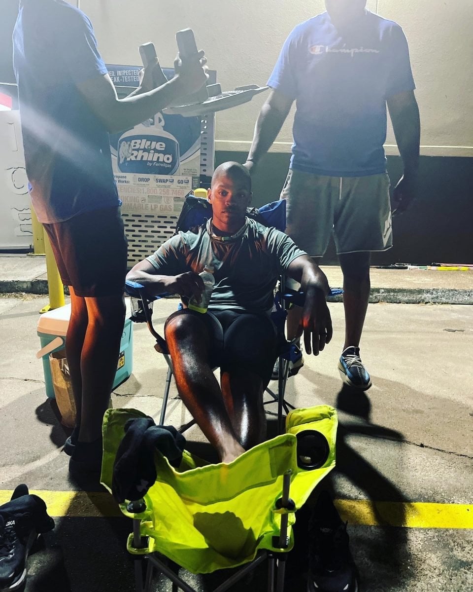 A man sitting in a chair taking a rest during a long race with support folks on either side of him