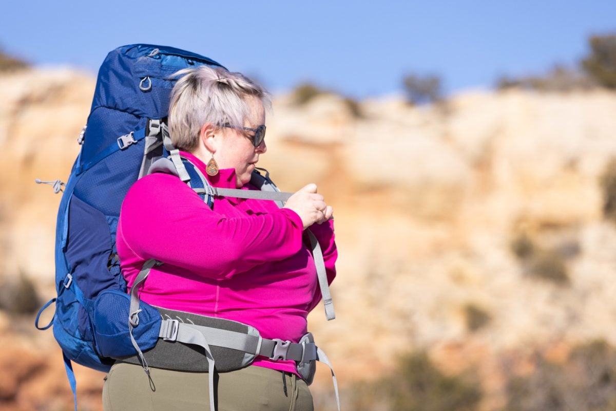 A woman wearing a blue backpack adjusting the sternum strap