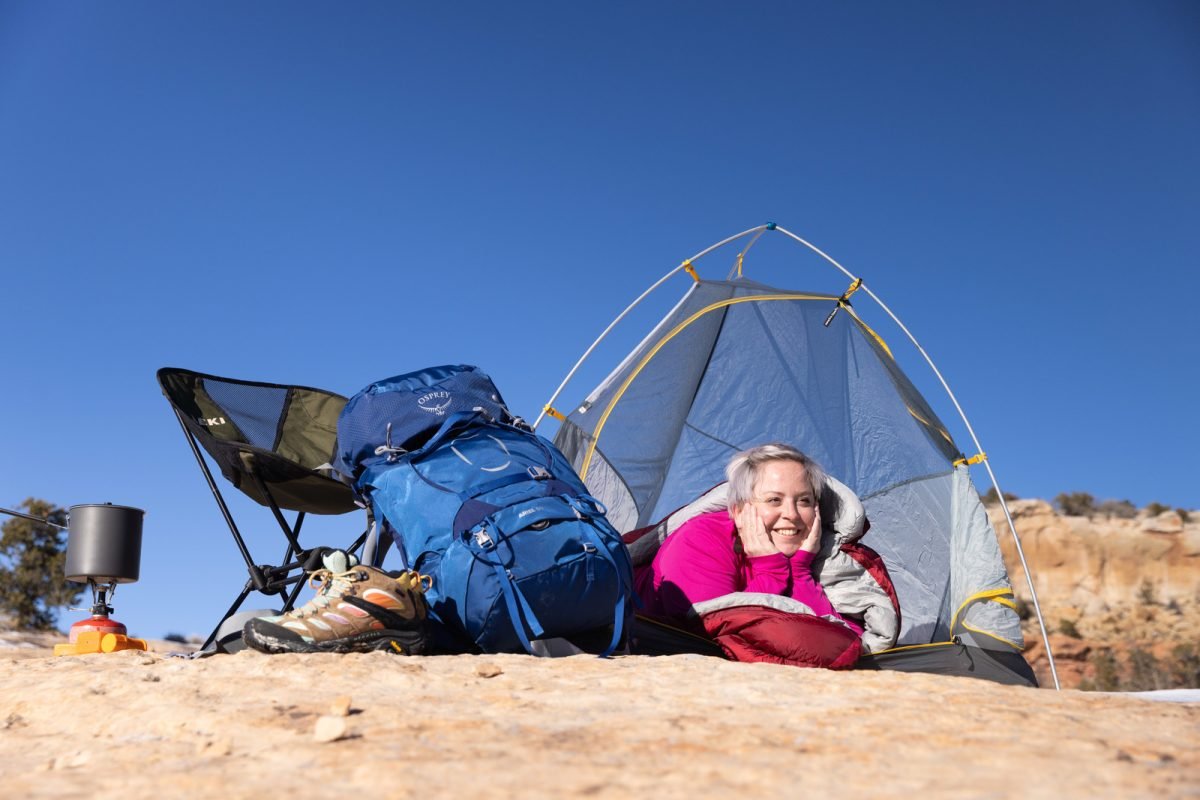 A woman laying in a tent facing out, with backpacking gear stashed to the side