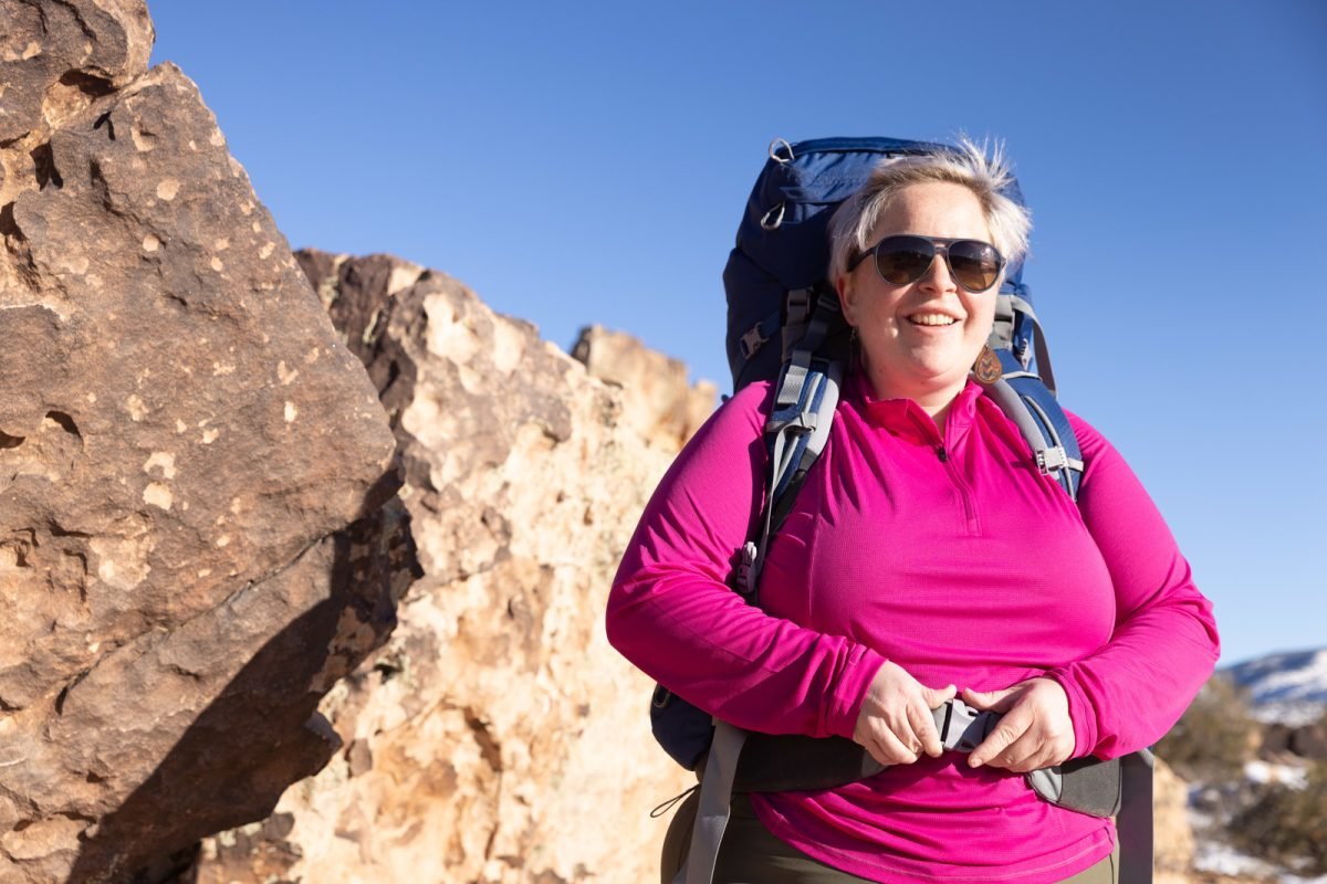 A woman wearing a pink shirt and a blue backpack adjusting her hipbelt strap