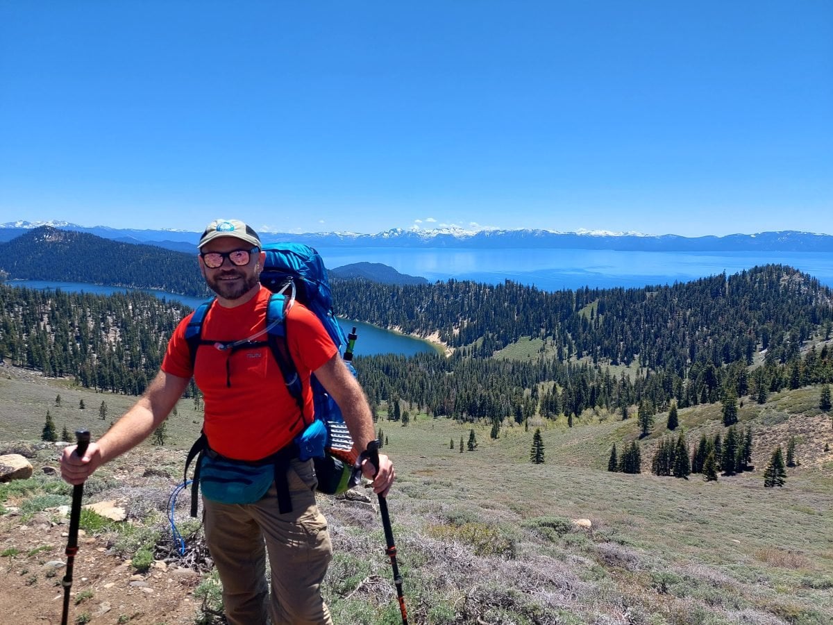 A man in backpacking gear posing with a landscape view of Lake Tahoe in the background