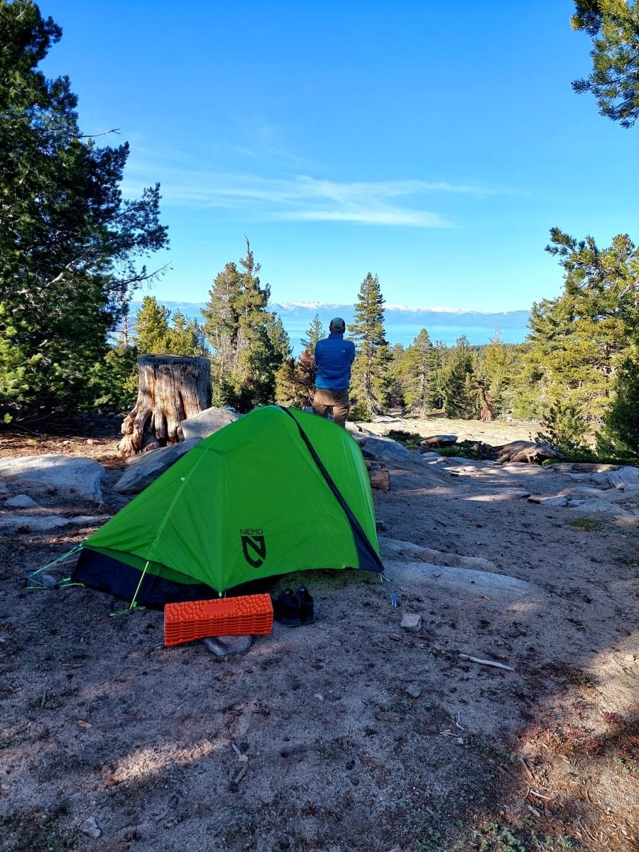 A man standing overlooking the lake, with camp set up in the foreground