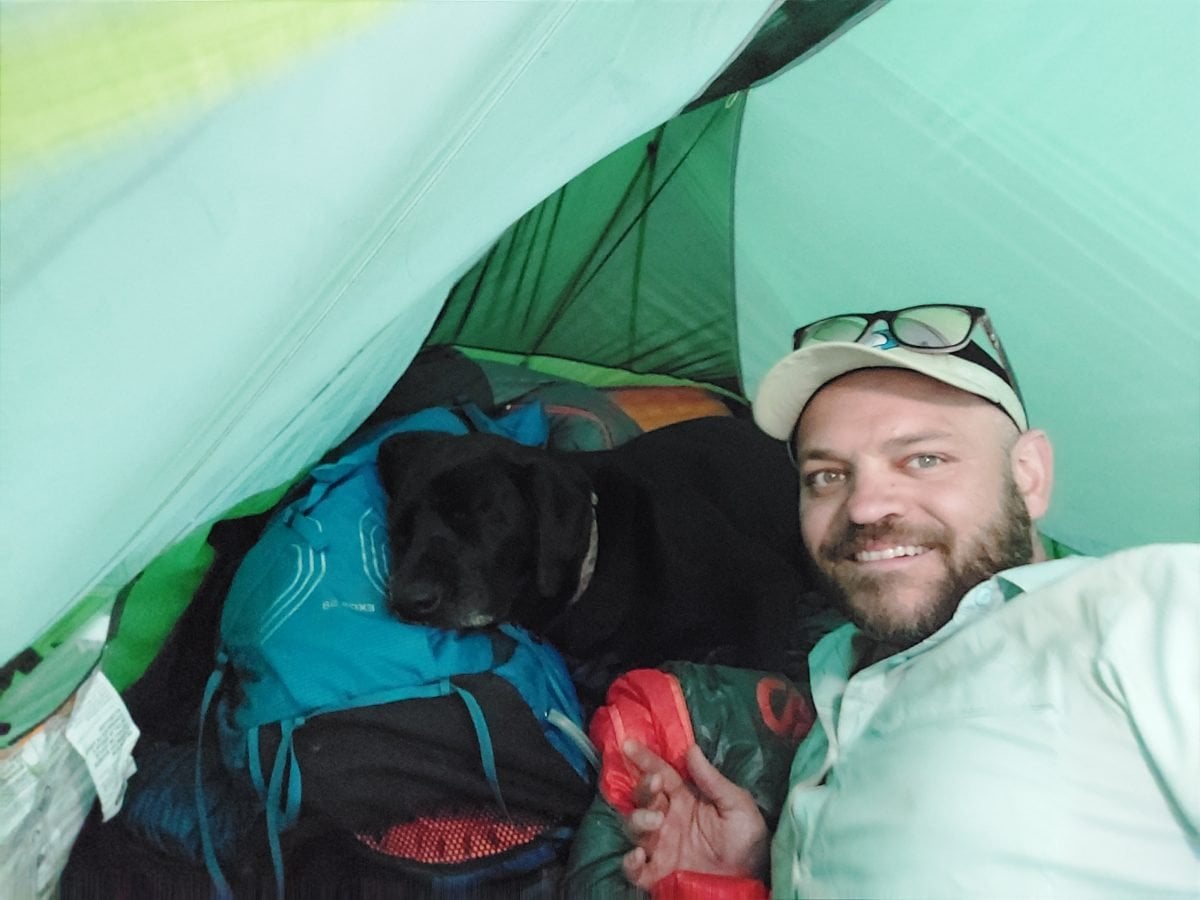 A man and his dog in their tent, surrounded by backpacking gear