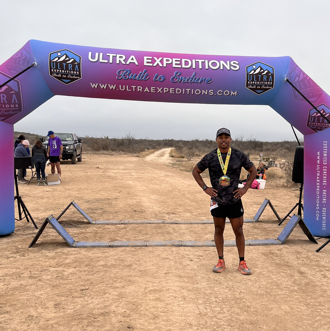 A man standing under a race finish setup, wearing a medal