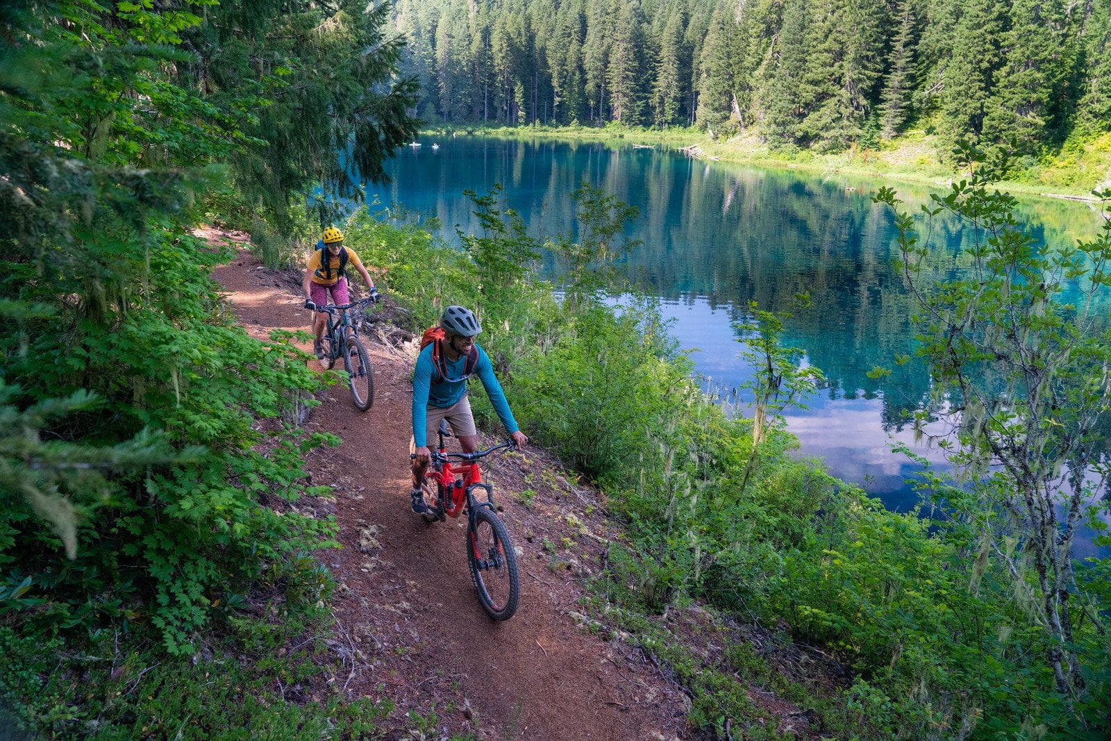 Two mountain bikers on a forested trail near a river