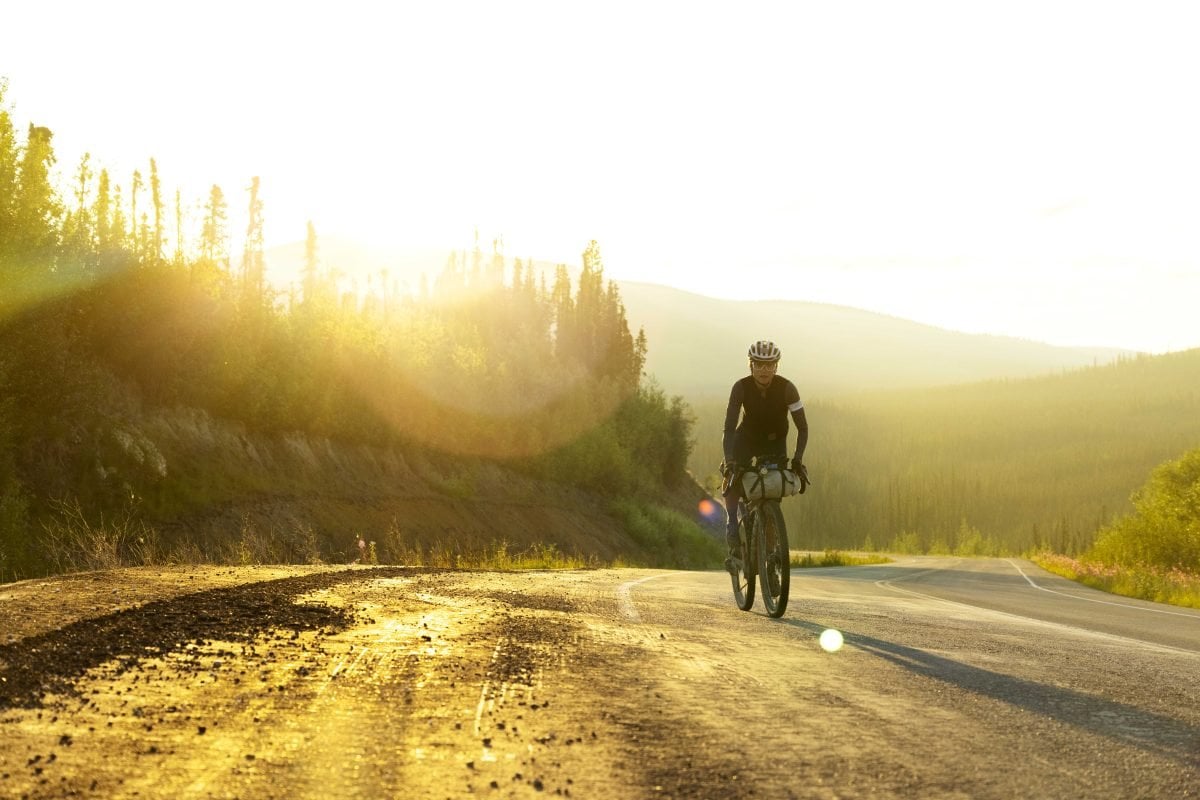 A person riding a bike alongside a road, with the sun shining in the background