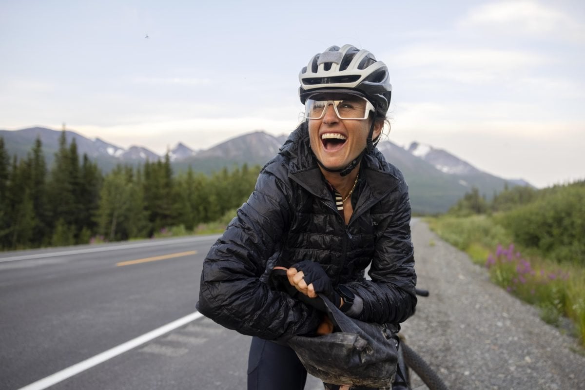 A person on the side of the road on a big, reaching in to a bag, smiling