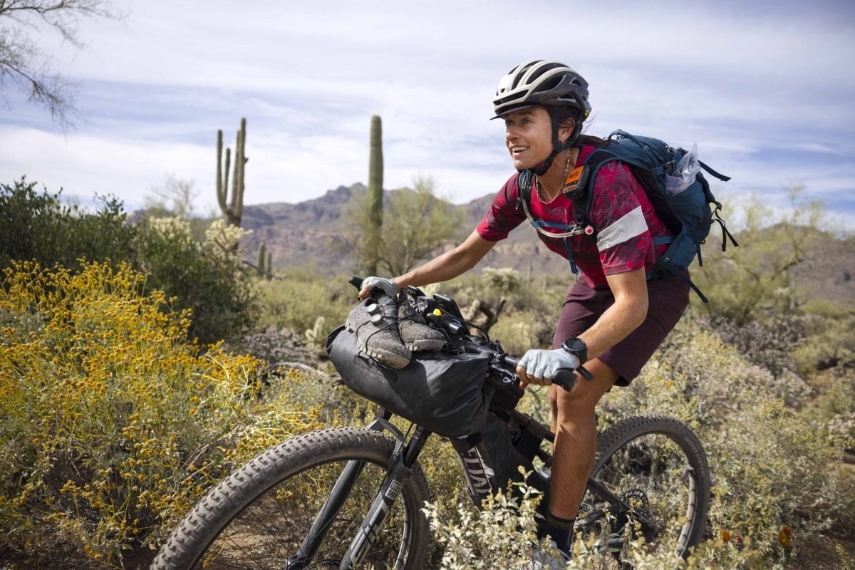 A person on a bike in the desert, with an on-bike bag and wearing a backpack