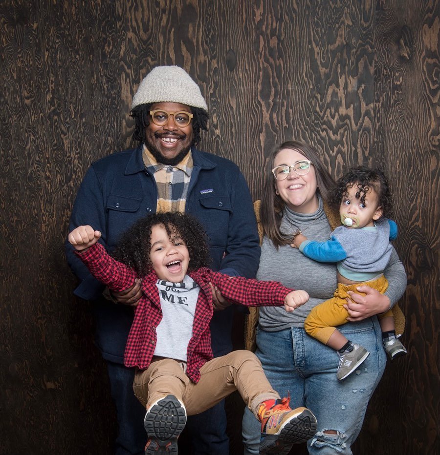 A family of four standing together in front of a wooden background