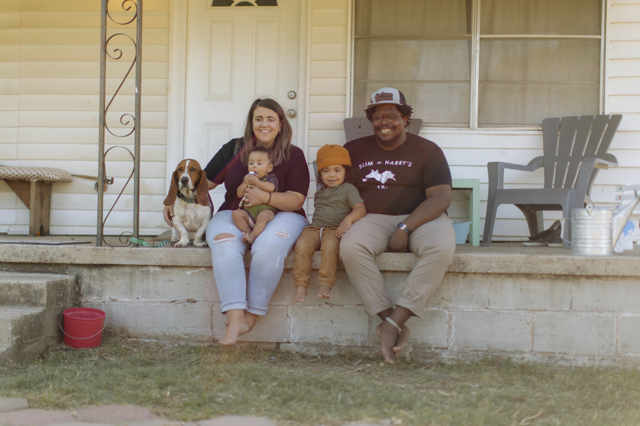 A family of four sitting on the porch together with their basset hound pup