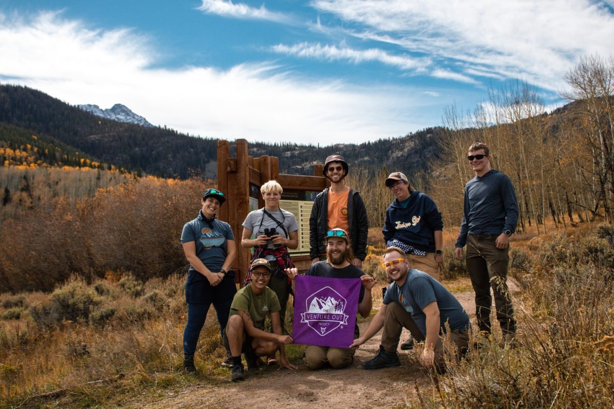 Eight people standing along a trail, with the middle person in the second row holding a TVOP flag
