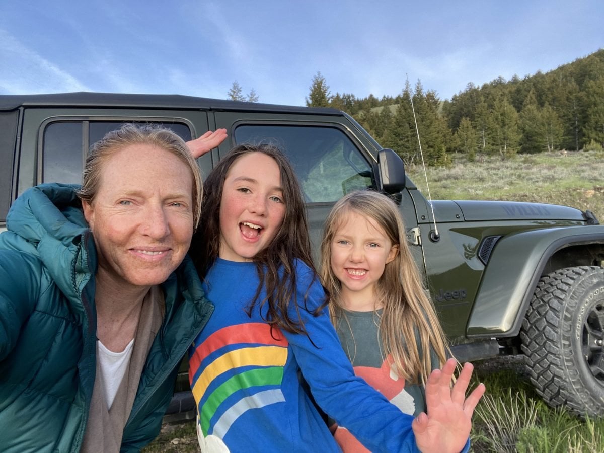A woman with her two kids outside, a green Jeep in the background
