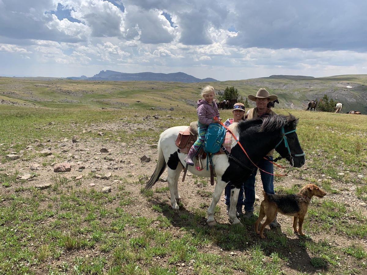 A man and woman standing next to their daughter on a horse, along with their dog