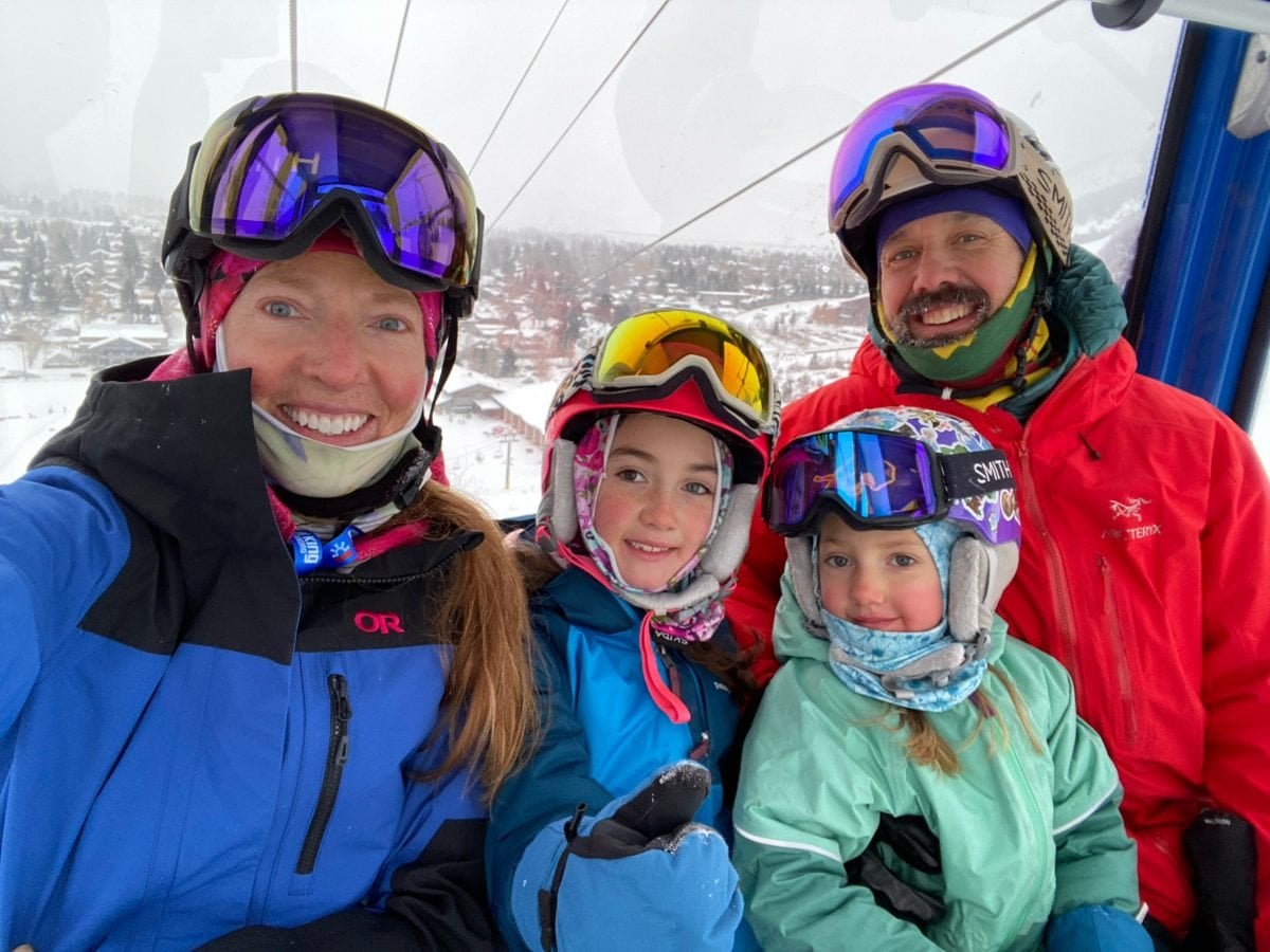 A man and woman in a gondola with their two kids, all wearing ski gear