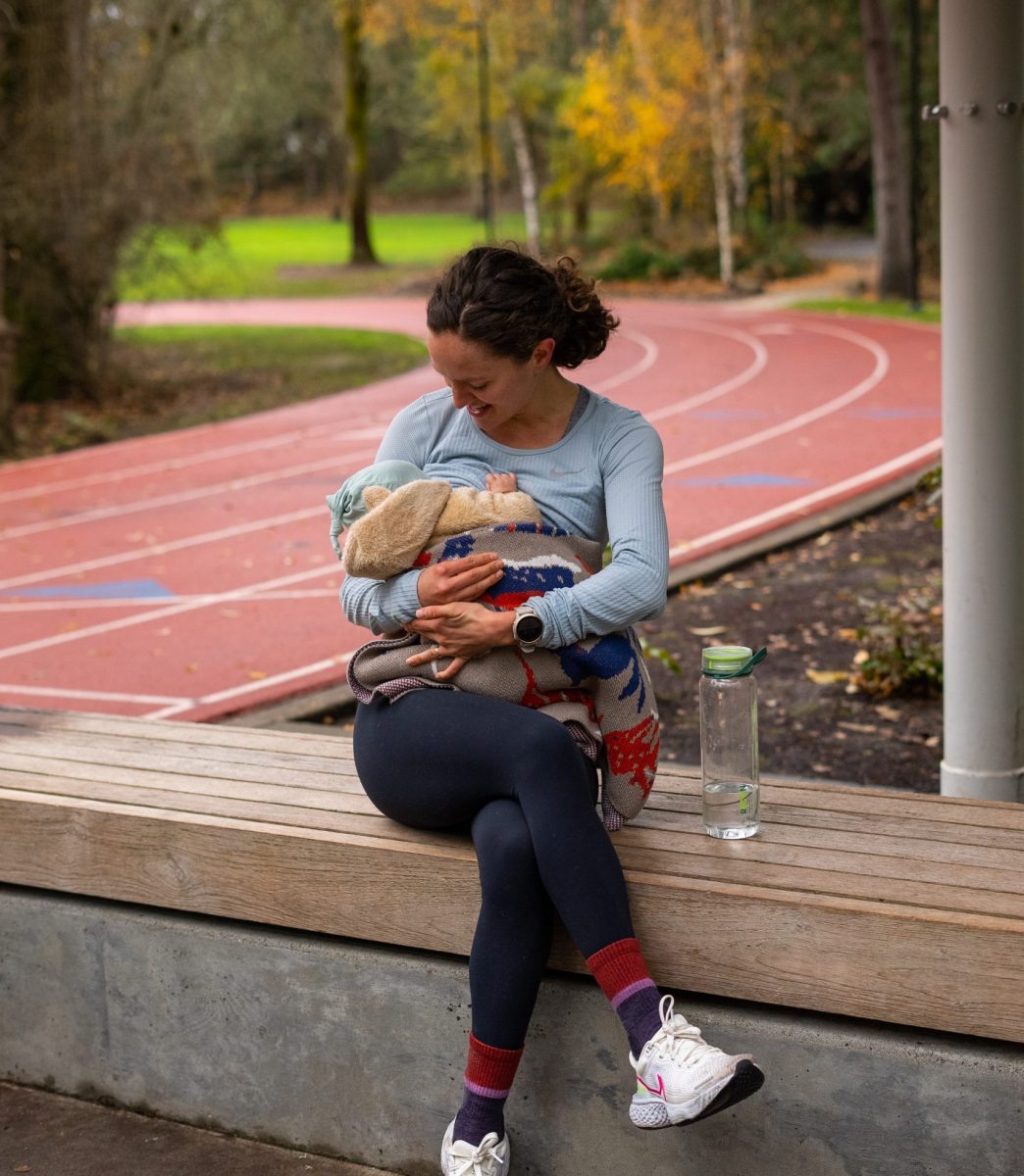 A woman sitting next to a running track holding her baby in her arms