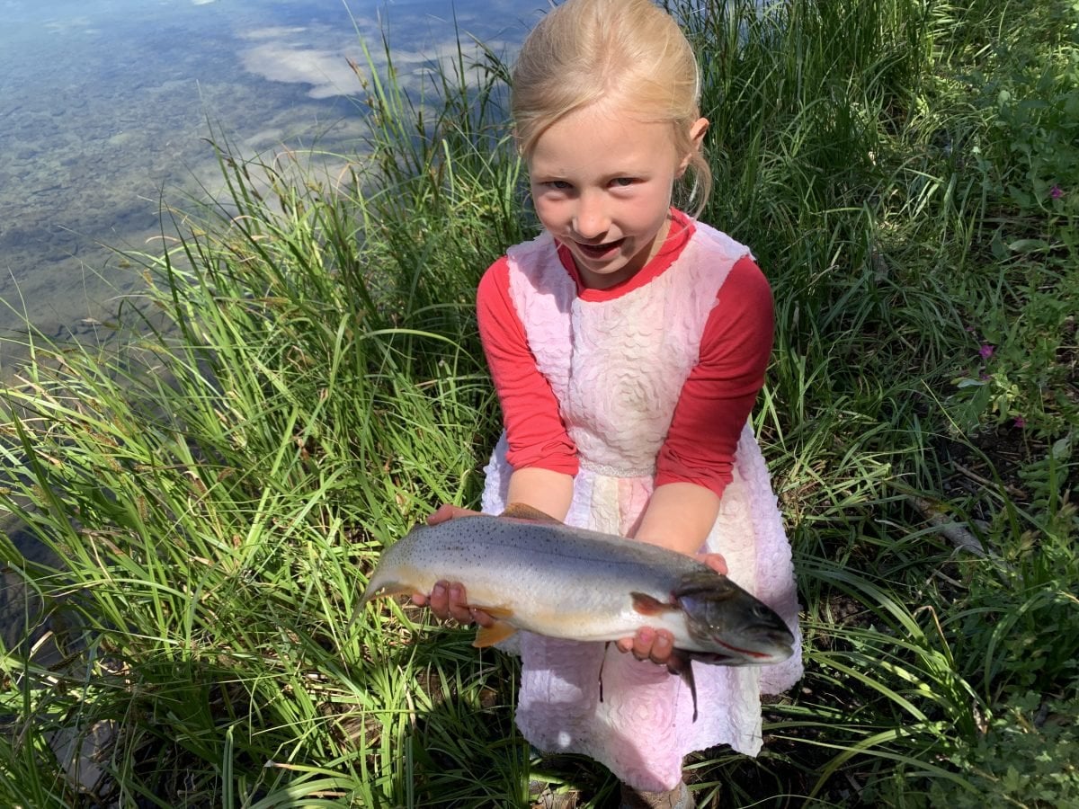 A small girl holding a fish in her hands next to a river