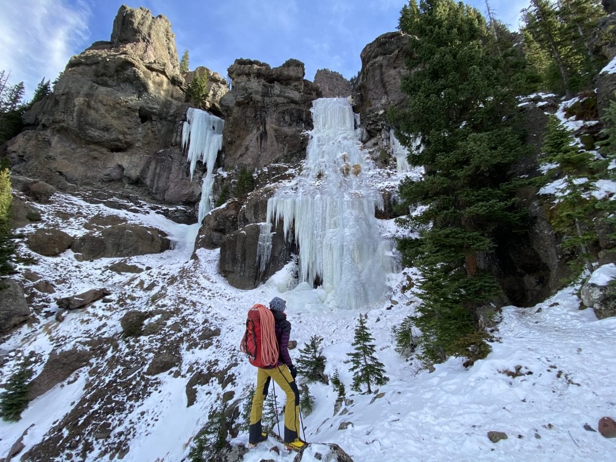 A woman standing at a frozen waterfall in full gear