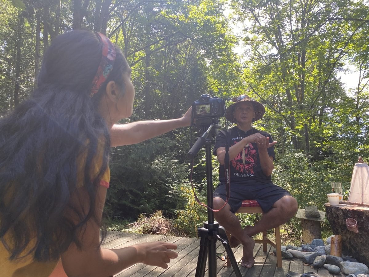 A woman with a camera on a tripod interviewing another individual sitting on a chair behind the camera