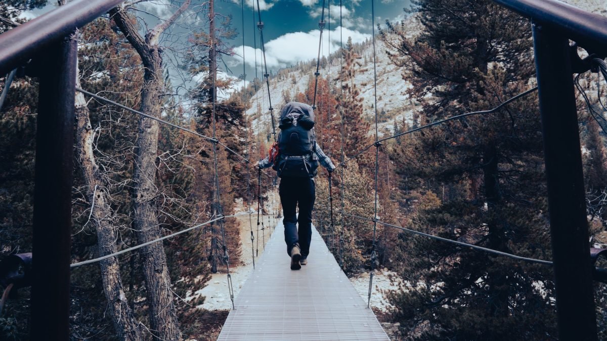 A person walking across a bridge, wearing backpacking gear