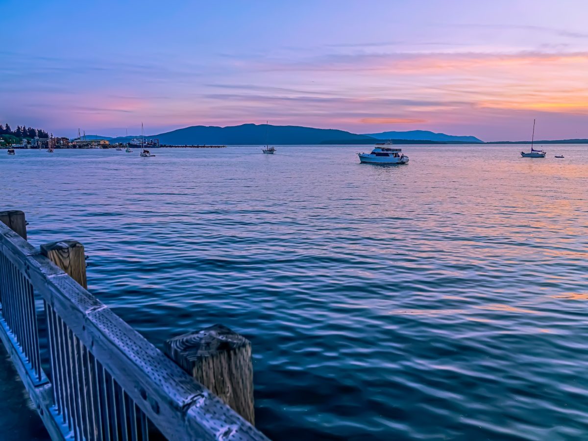 A view of a lake during sunset, with boats on the water and mountains in the distance