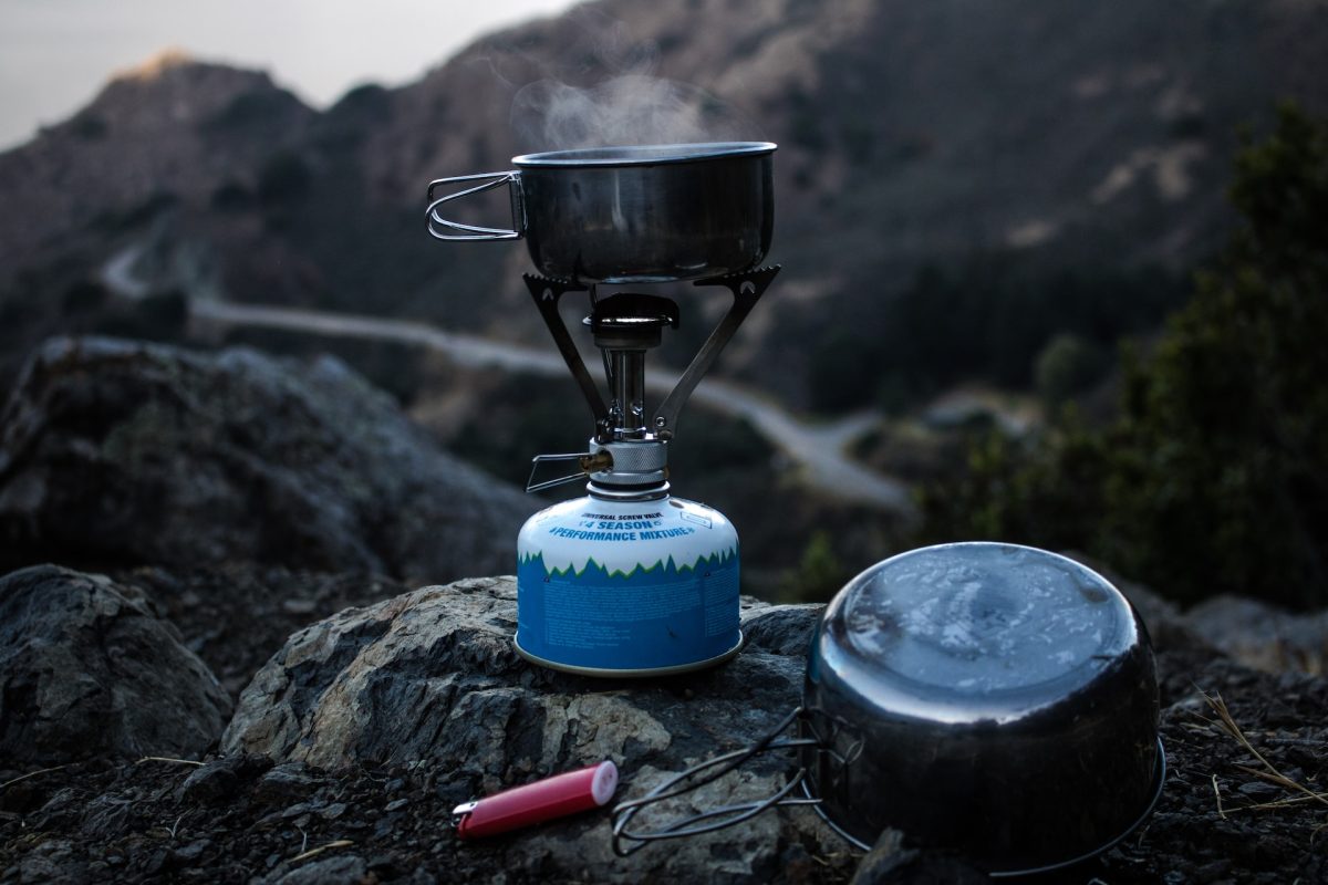 A camping stove setup atop a rock, with a trail in the background