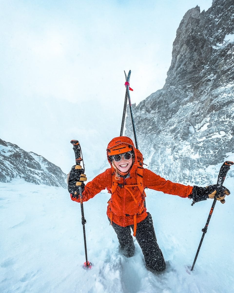 Osprey Athlete Madison Rose in full ski gear during an ascent, wearing orange and black gear, and a big smile