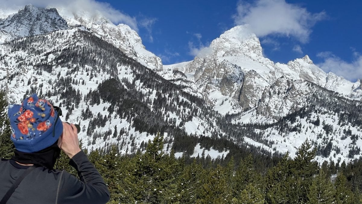 A person using binoculars looking out at the Grand Teton mountain range
