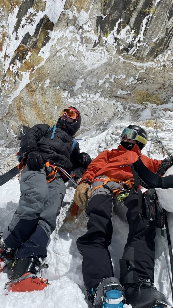 Two people in full ski gear looking up and away