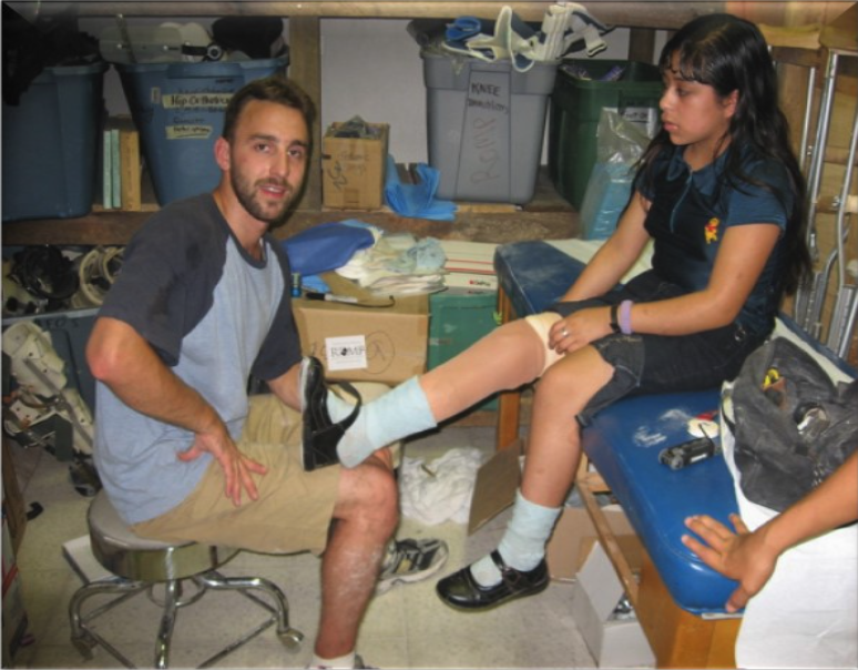 A man sitting with a younger girl who is sitting on a medical table getting fitted for a prosthetic leg.