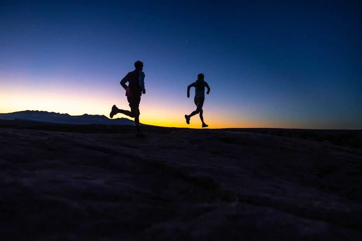 Two people running in silhouettes in a desert landscape
