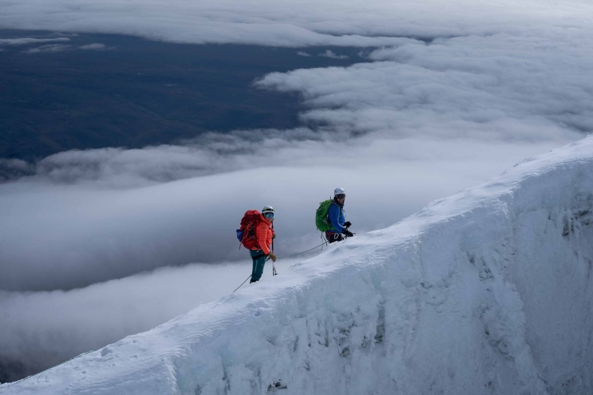 Two people in mountaineering gear climbing a snow-covered mountain