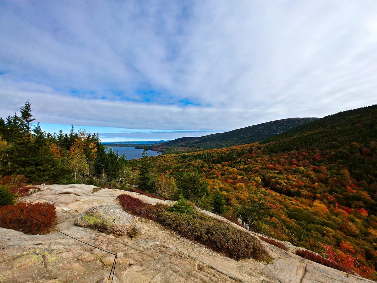 A landscape view of colorful trees and a body of water in the background from a rock overlook