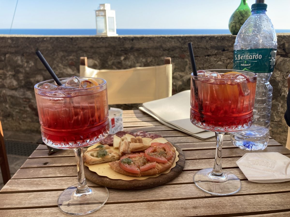 A table set with snacks and two aperol sprtizs; in tall-stemmed glasses