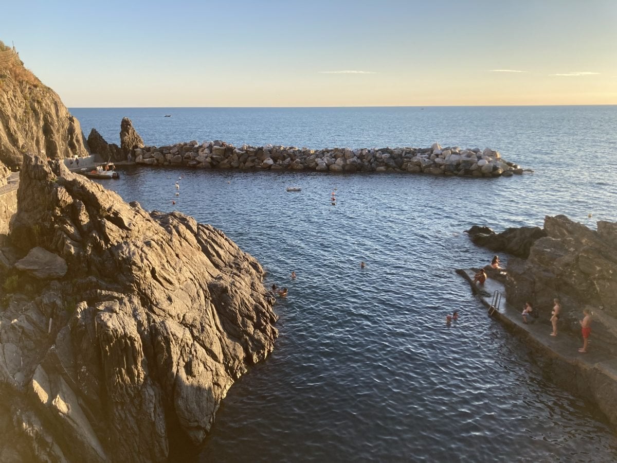 A landscape view of people cliff jumping off of either side of a pair of cliffs into the water