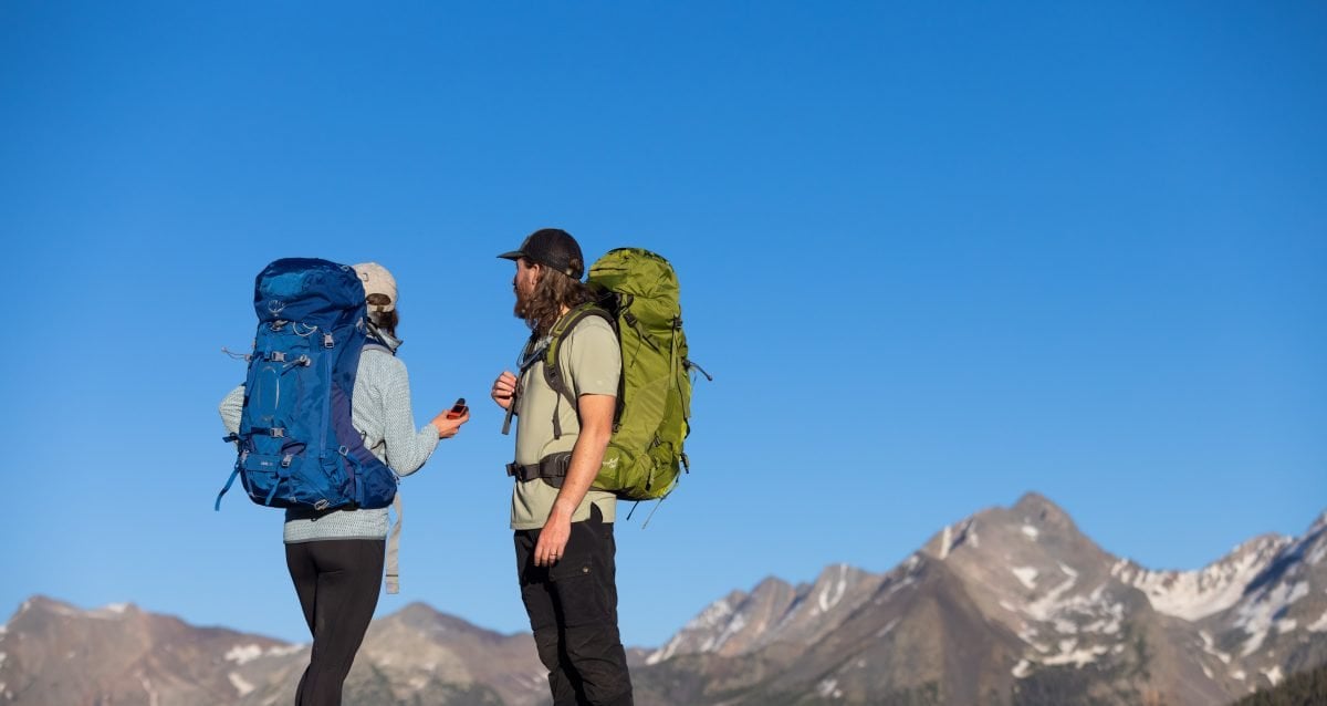 Two people standing in backpacking gear on a backcountry trail, with a Garmin inReach Mini, looking in the distance