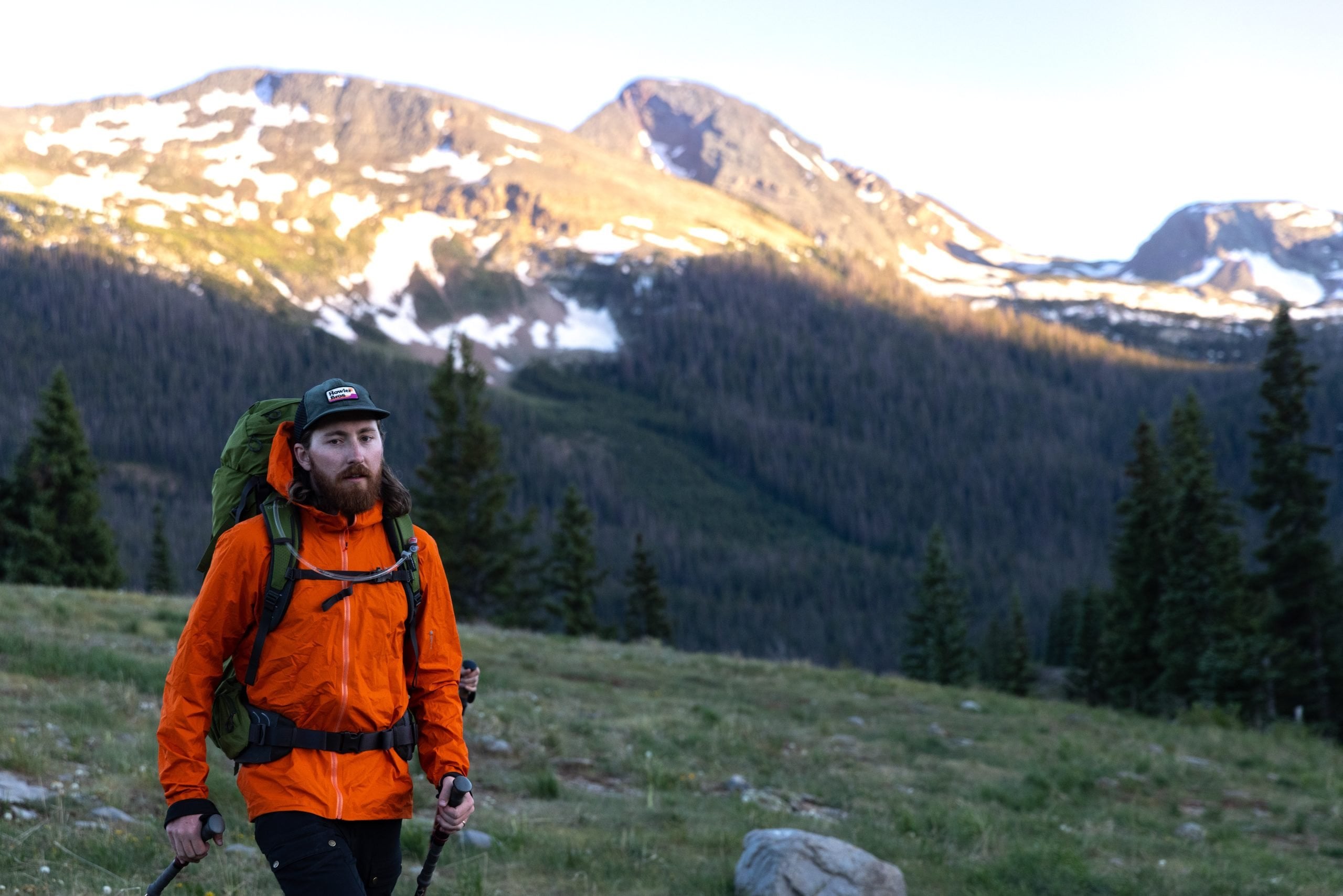 A man walking along a backpacking trail in the backcountry in full gear, and an orange jacket