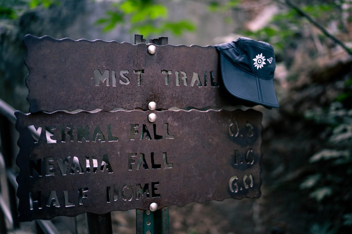A trail sign, with a black Latino Outdoors hat sitting atop the sign