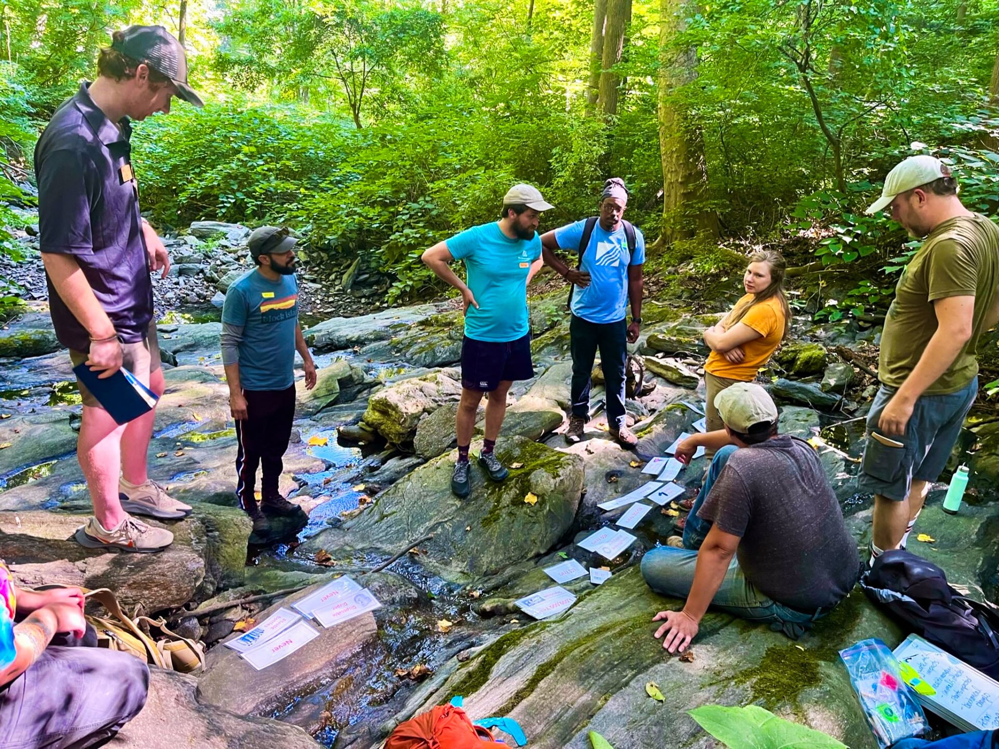 A group of people gather in a river bed sorting note cards.