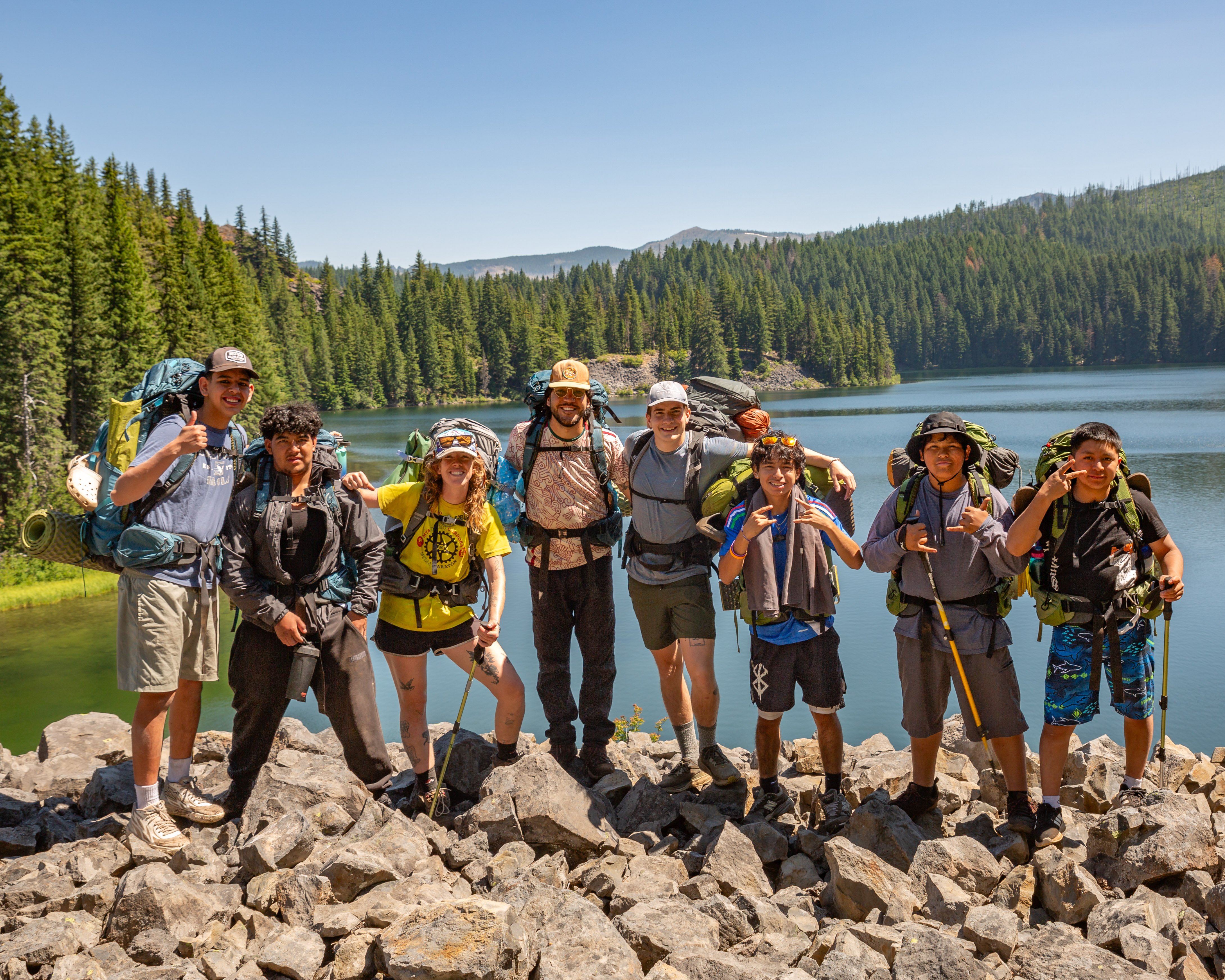 A group of backpackers standing together on a rocky ledge, with a body of water in the background