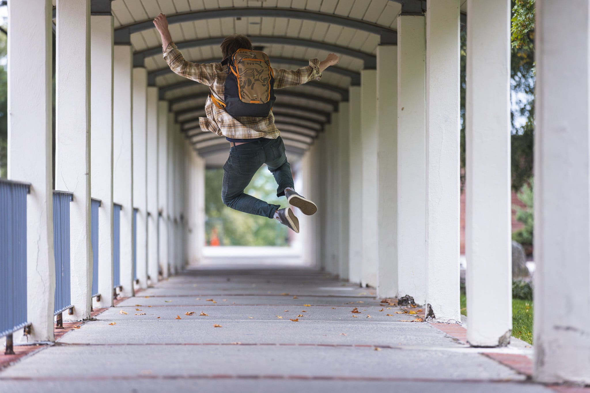 Student jumping with a backpack on in a school courtyard.