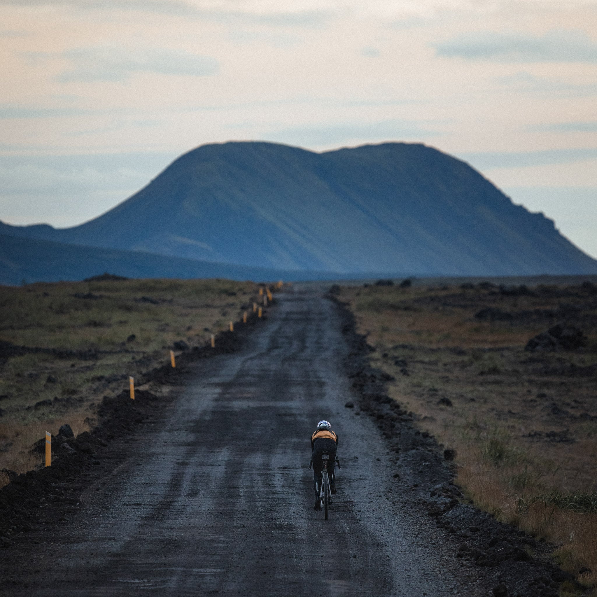 A cyclist rides down a road toward the mountains.