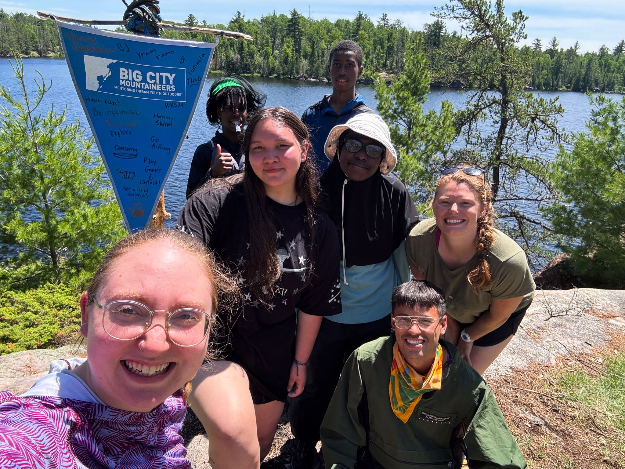 A group poses with a Big City Mountaineers flag by the water.