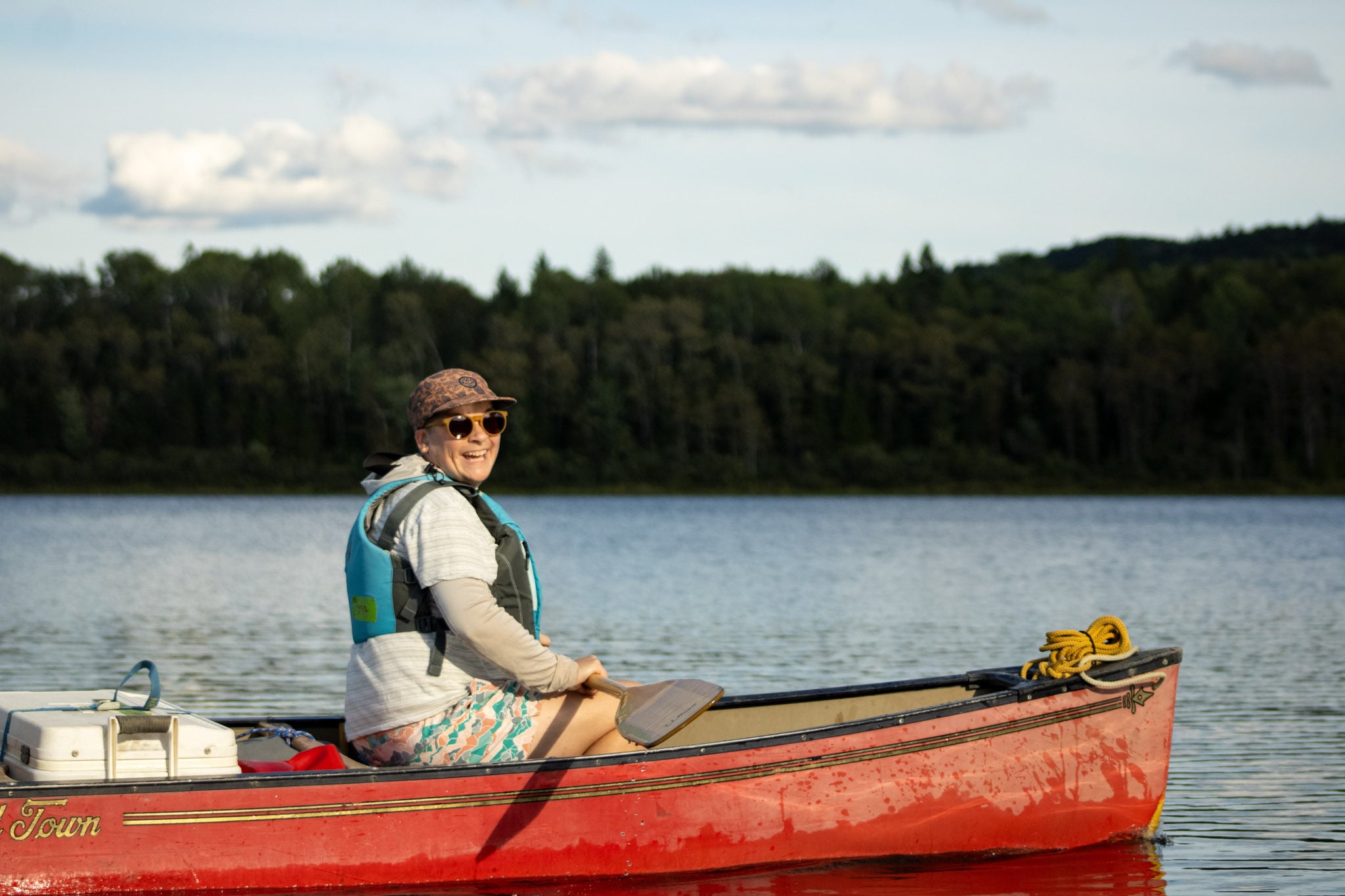 A person sits in a red canoe on a lake smiling at the camera.